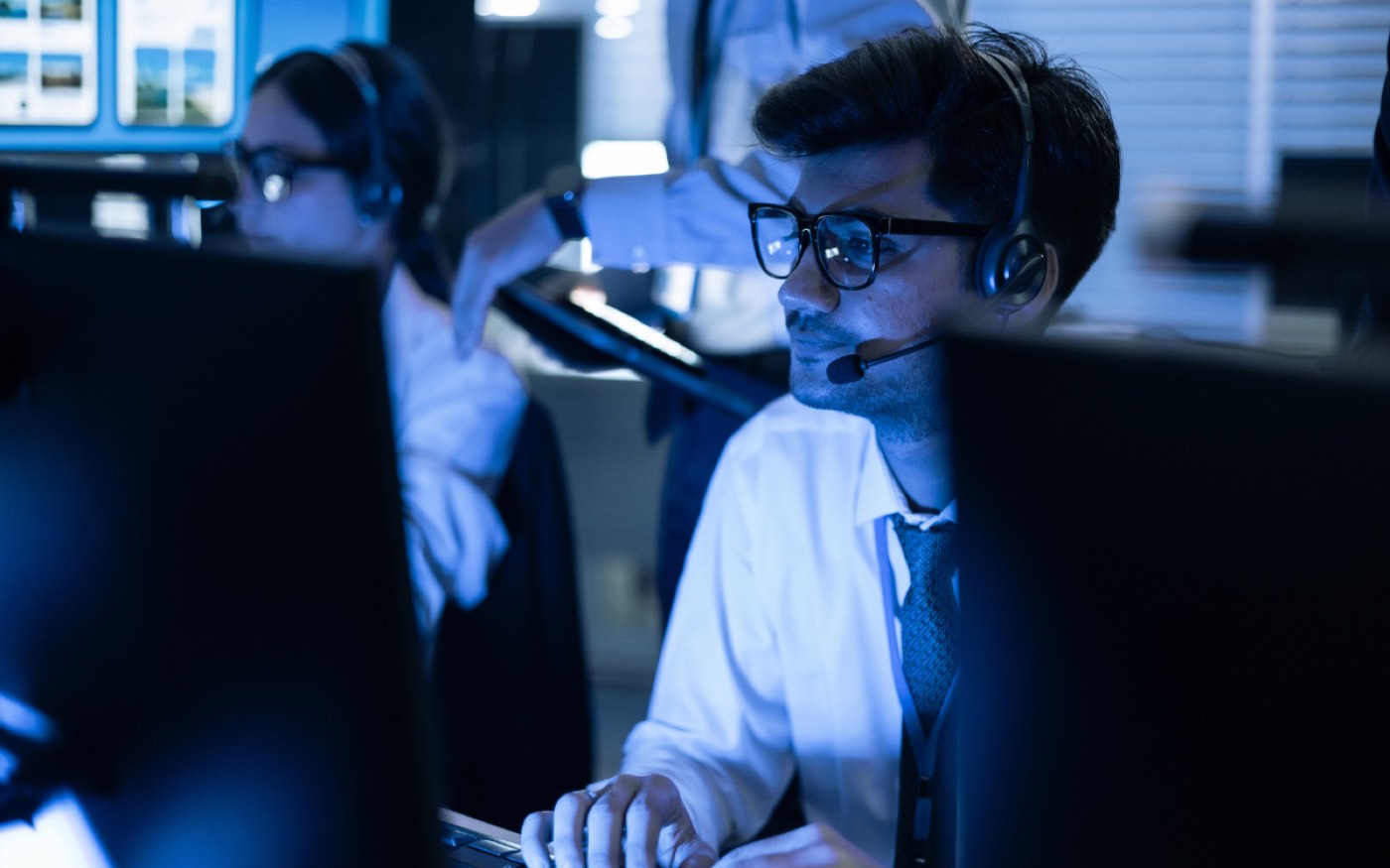 Two security analysts working at monitoring stations in a darkened operations room